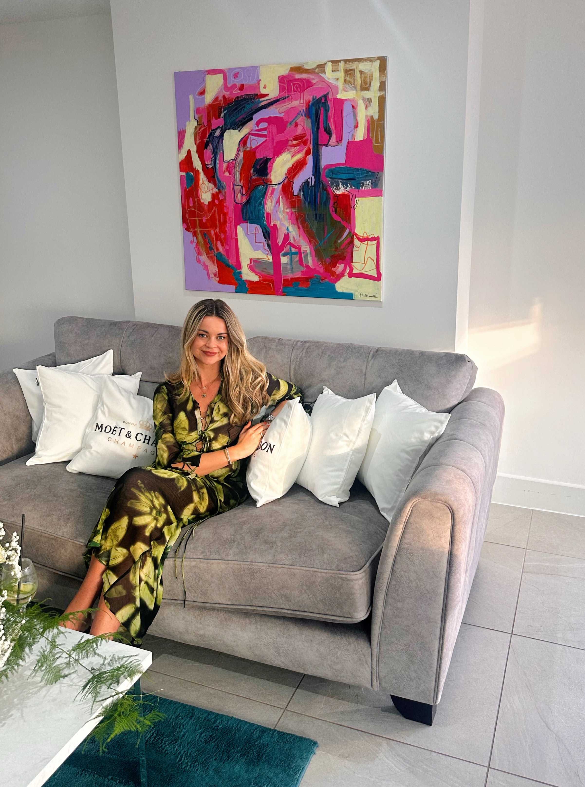 Image of Harriet sat on a sofa with her painting The Night Before hanging above her